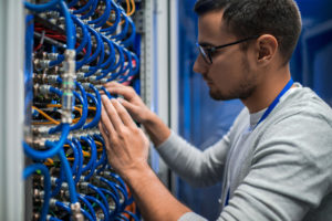 Side view portrait of young man connecting wires in server cabinet while working with supercomputer in data center